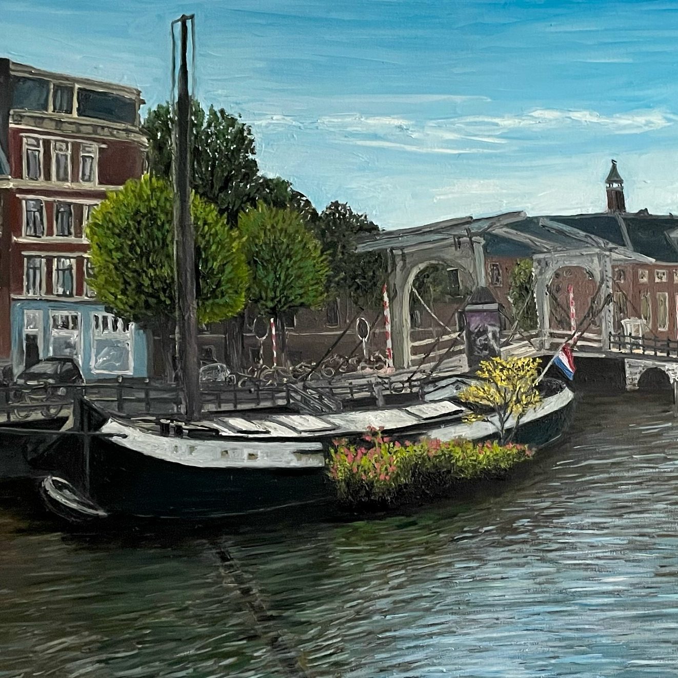 A moored Canal boat in Amsterdam with flowers, surrounded by buildings and trees by a river.